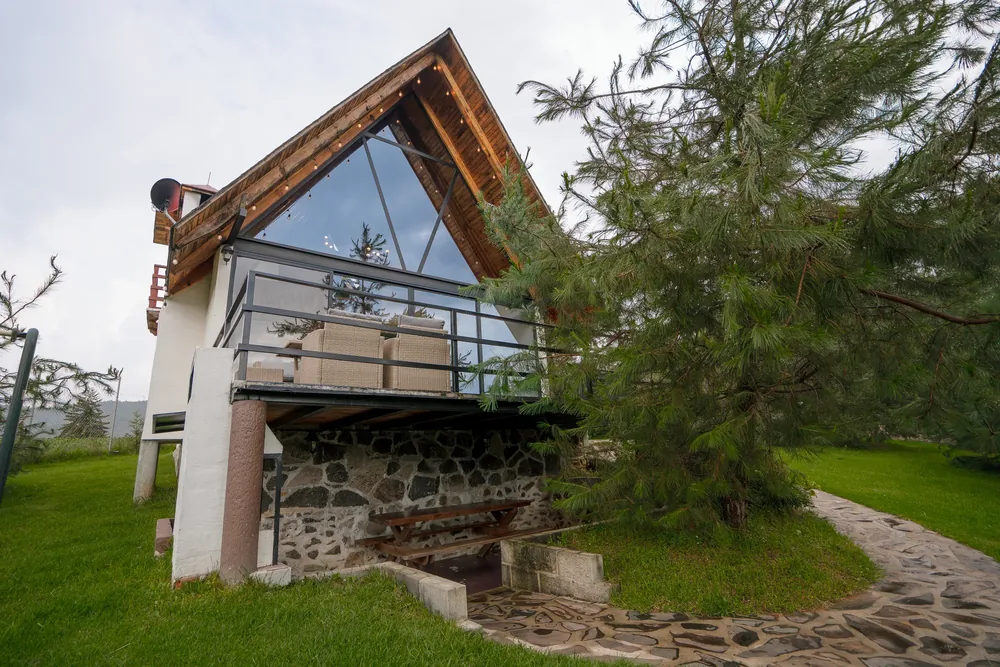 Cabaña Centauro estilo A-frame con frente de cristal y base de piedra